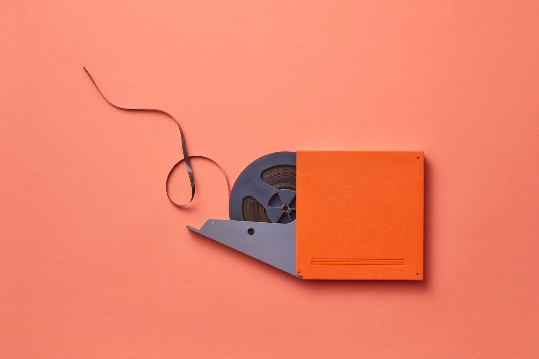 Close-up of a vintage film reel on a vibrant orange background with tape exposed.