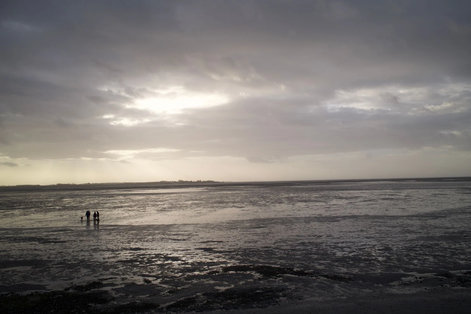 People walking along a coastal shore at low tide under dramatic skies.