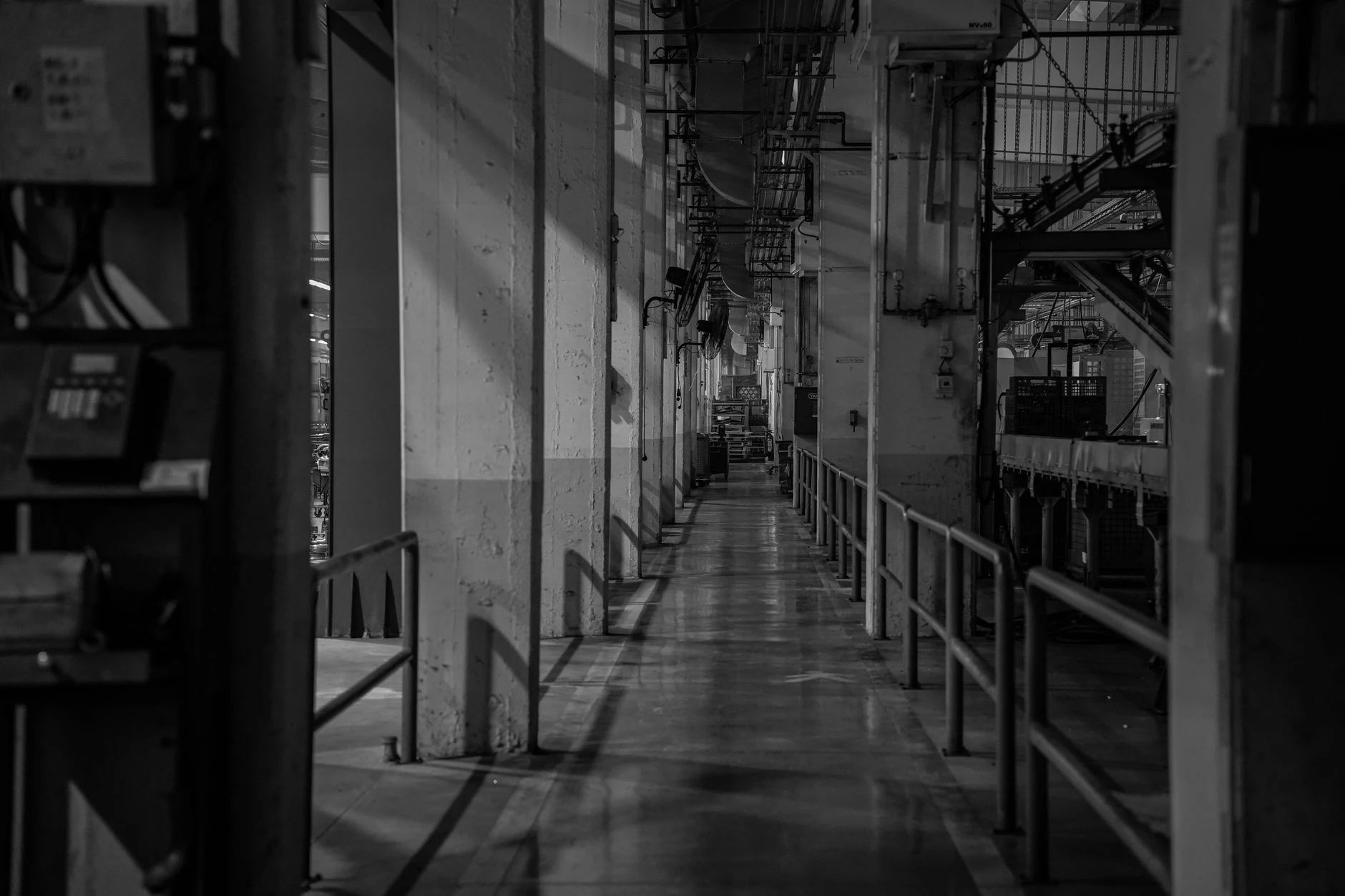 A dramatic black and white view of an empty industrial corridor with shadows.