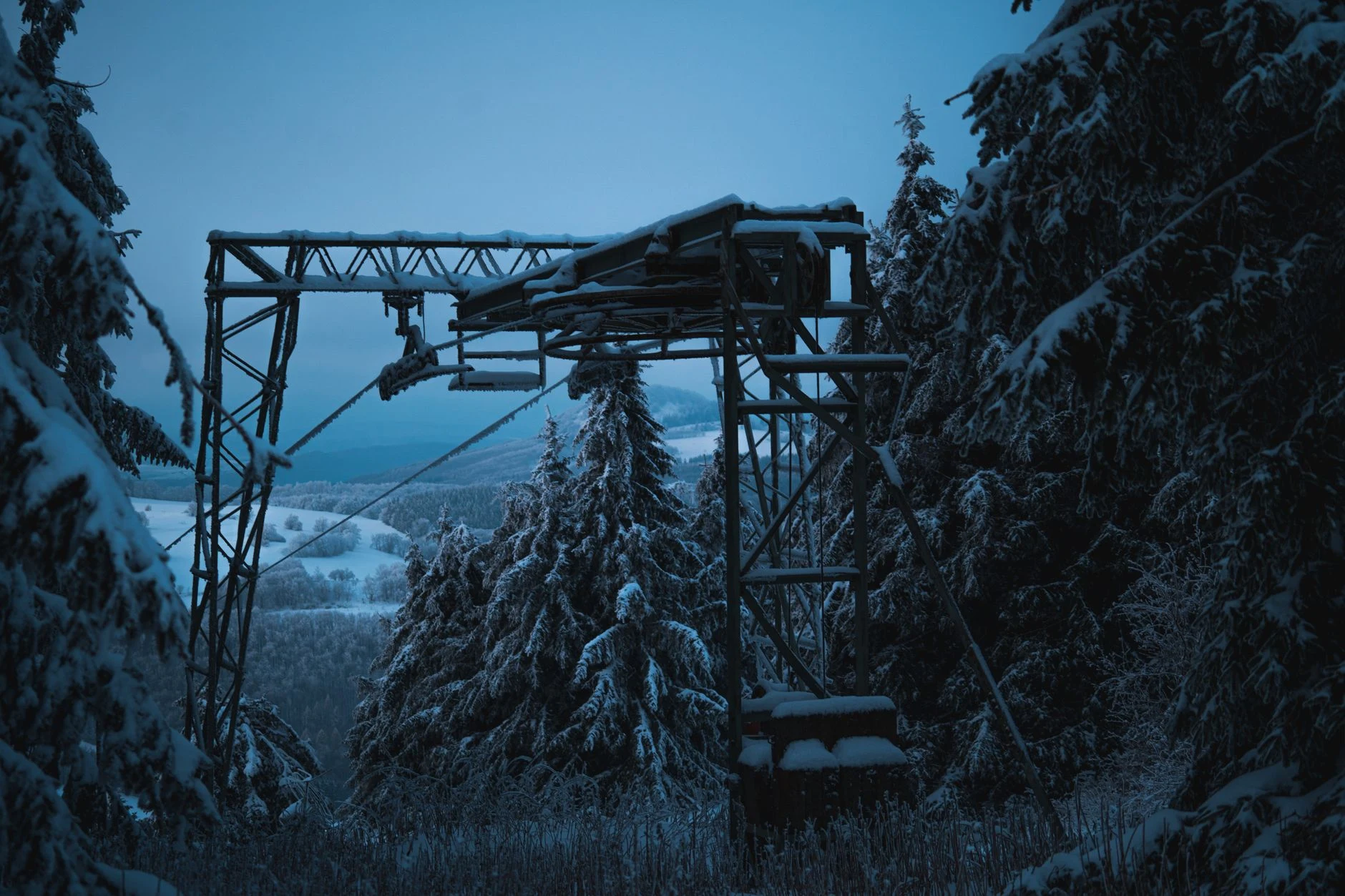 A snowy cable railway structure amidst winter forest conifers under a blue sky.