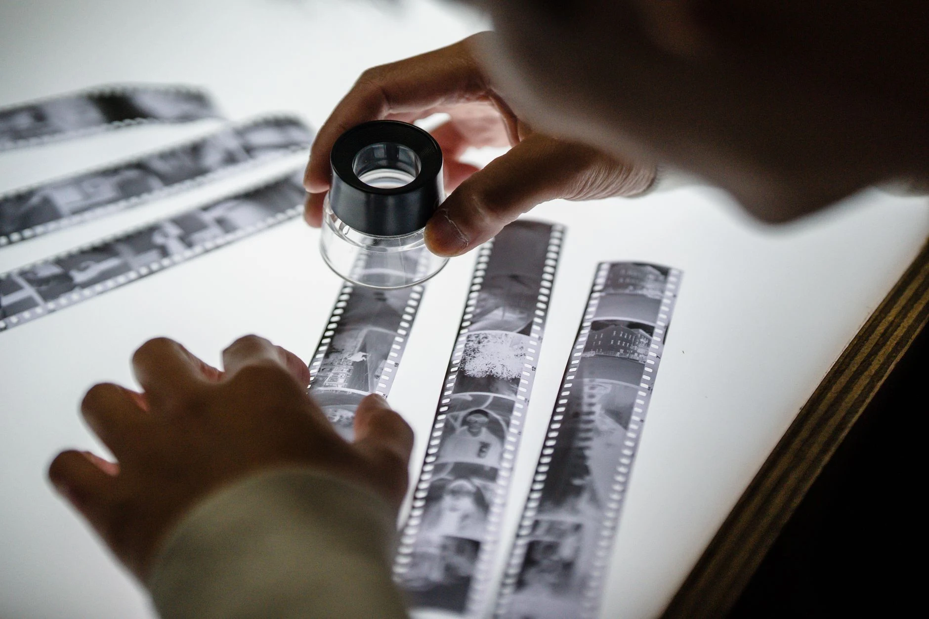 Hands examining film negatives with a magnifier on a light table.