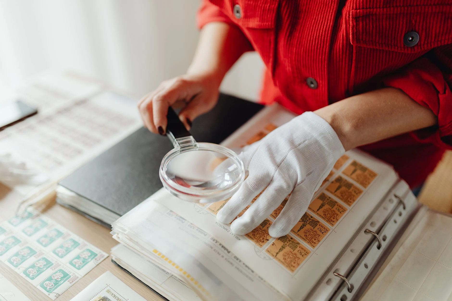 Close-up of a person examining stamps with a magnifying glass and gloves.