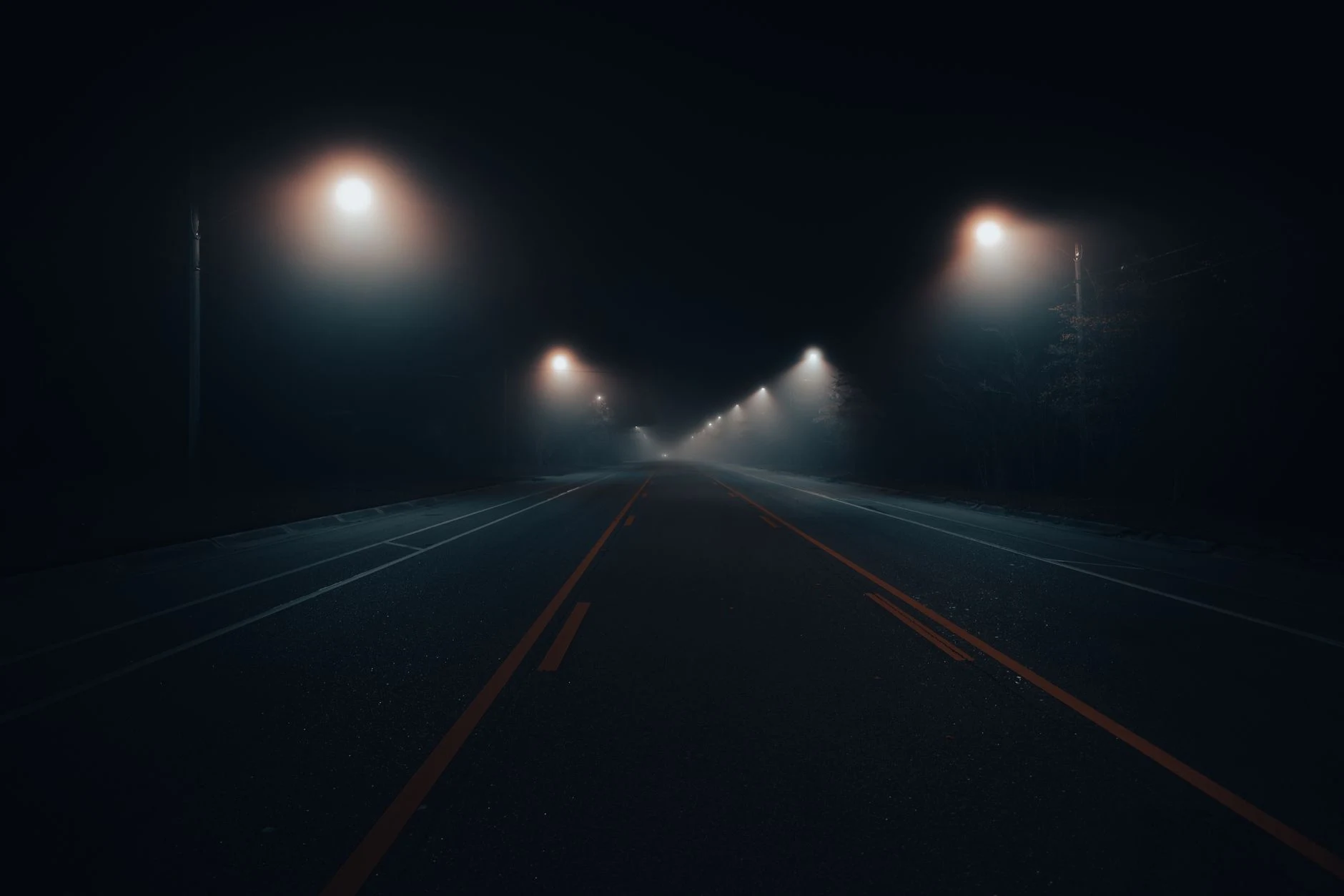 Foggy road illuminated by streetlights at night, capturing an eerie urban atmosphere.
