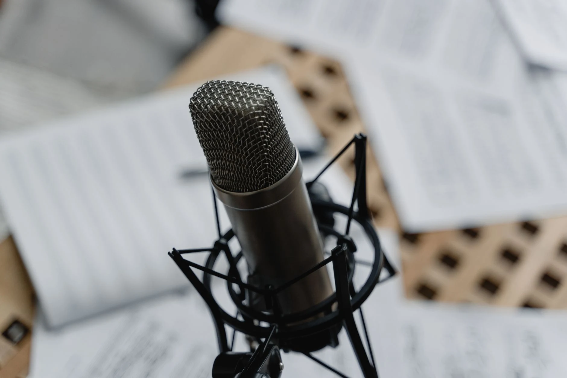 Close-up of a condenser microphone on a mic stand surrounded by music sheets in a studio setting.