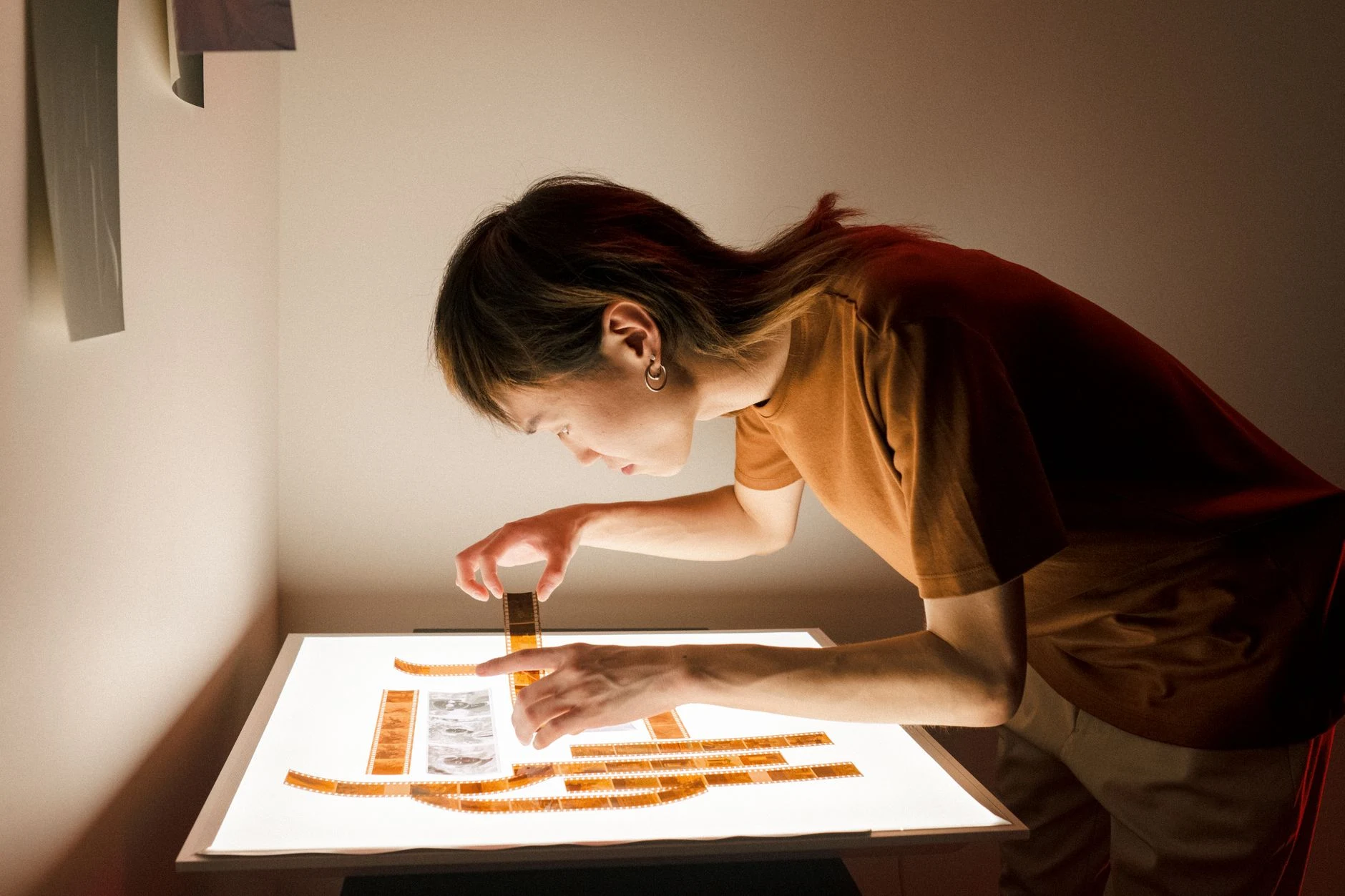 A photographer inspects film negatives on a light table in a dimly lit room.