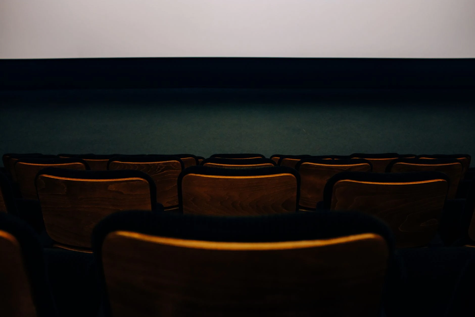 An empty auditorium with wooden seats facing a blank theater screen.