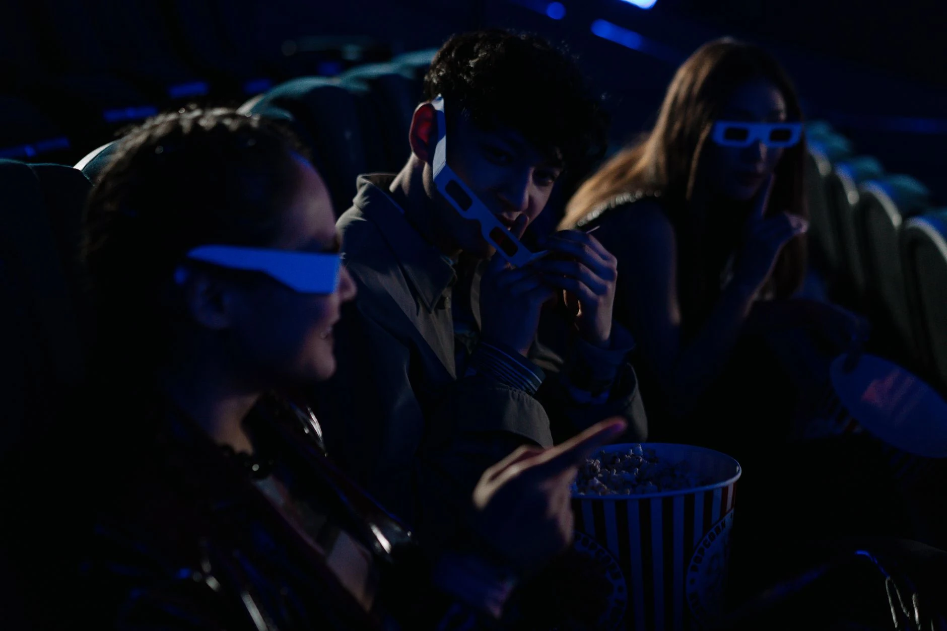 Friends wearing 3D glasses enjoy popcorn and movies in a cinema theater.