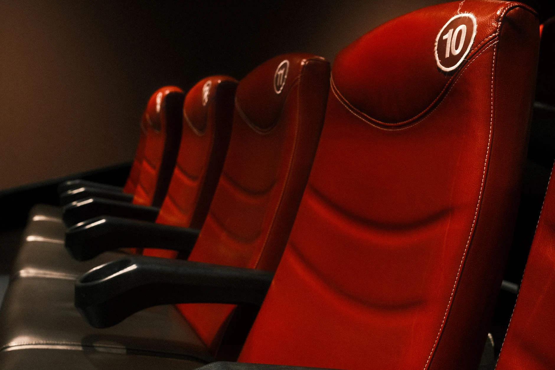 Row of plush red cinema seats with armrests in a dimly lit theater.