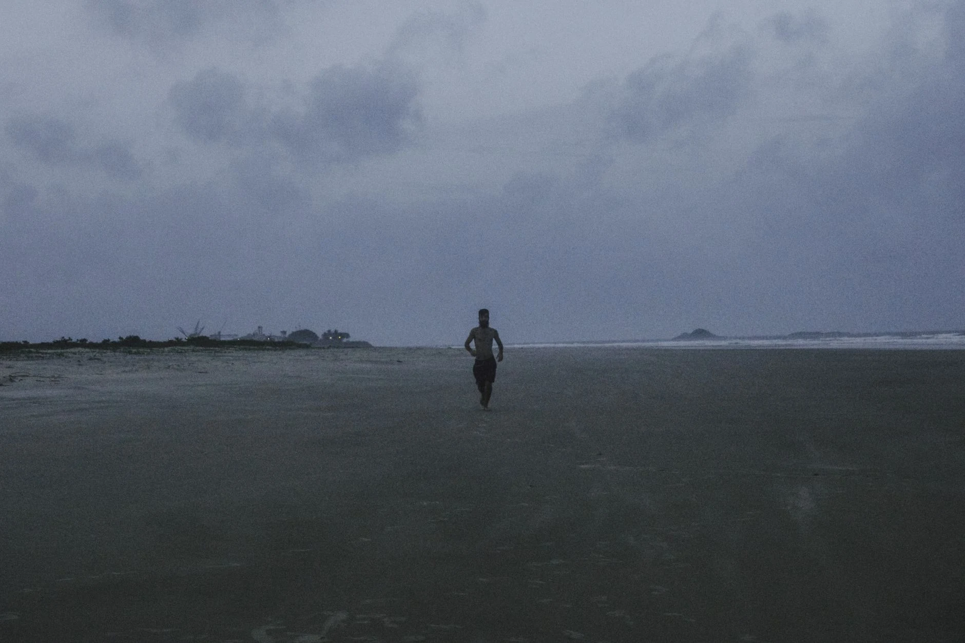 Person walking on an empty beach in Ilhéus, Brazil during twilight.