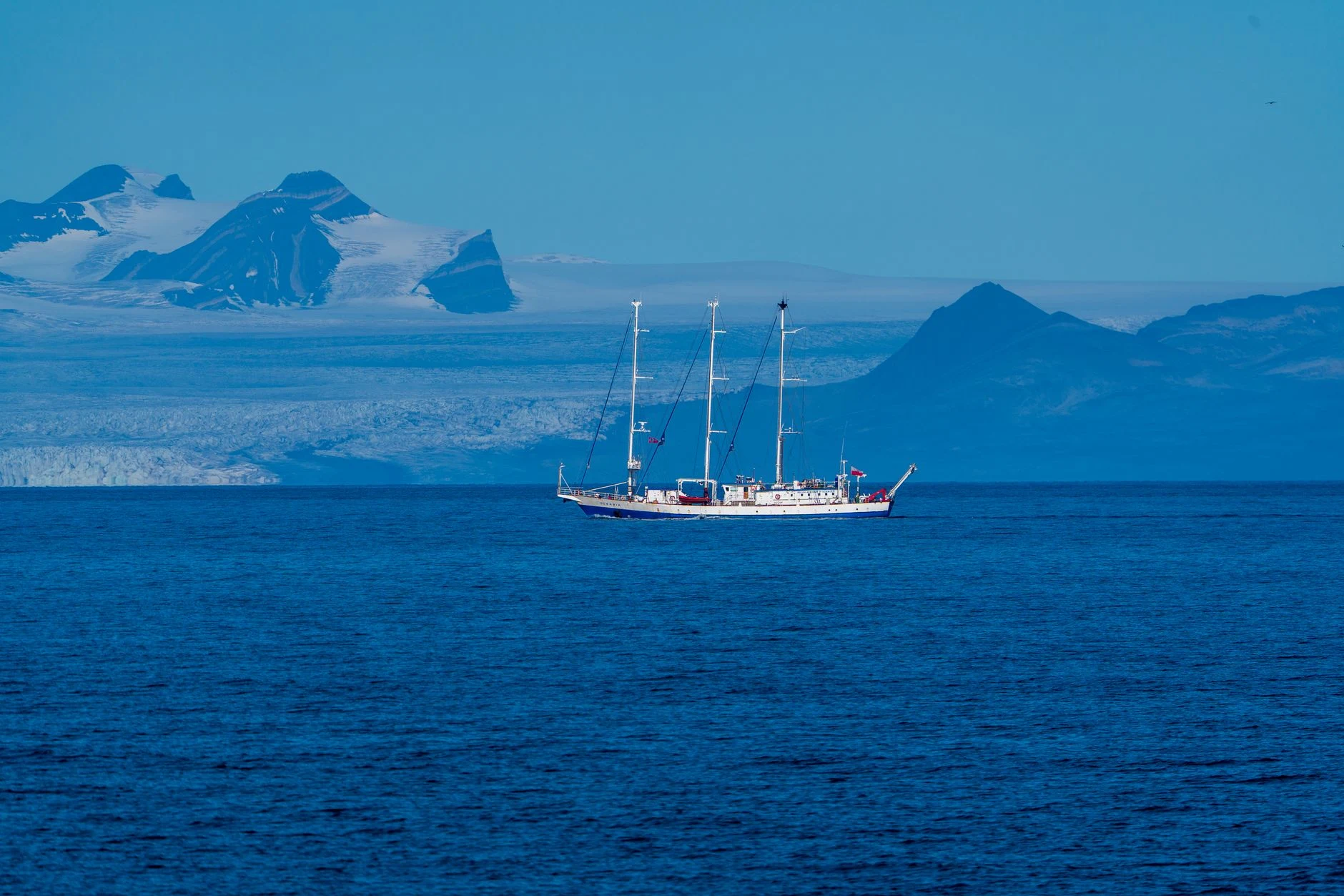 A majestic sailing ship navigating the icy waters of the Arctic near Svalbard's rugged mountains.