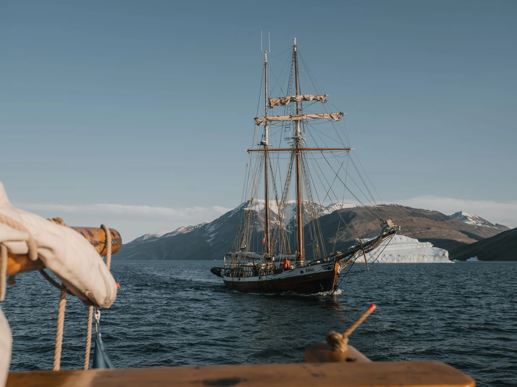 Historic sailing ship in the Arctic, mountains and iceberg in the background.