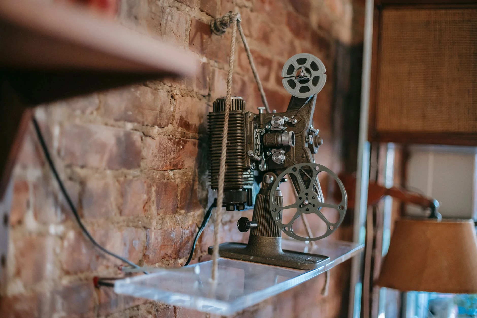 Retro film projector placed on glass shelf near brick wall in cozy apartment