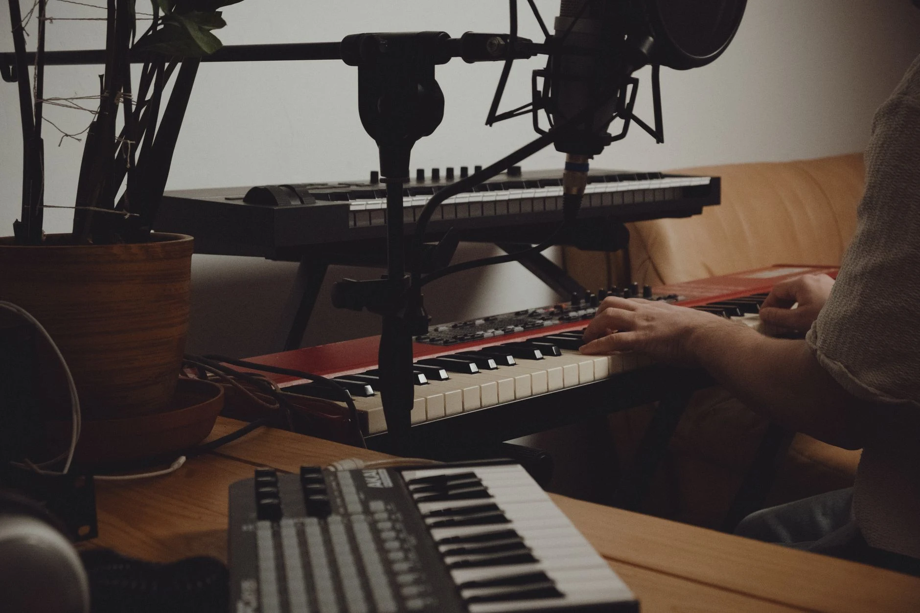 Person playing keyboard in a home music studio with recording equipment.