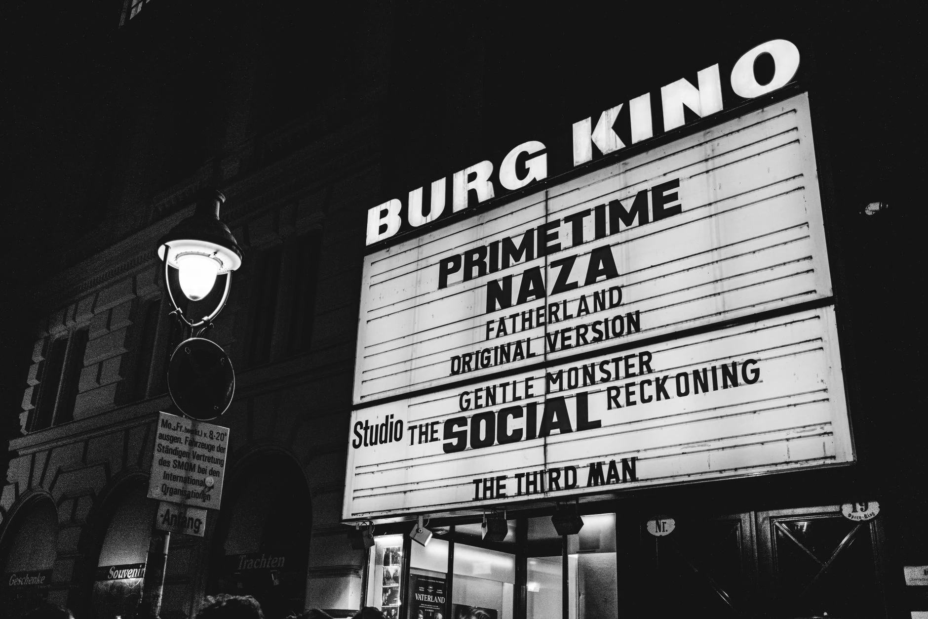 Black and white photo of Burg Kino cinema marquee in Vienna displaying movie titles at night.