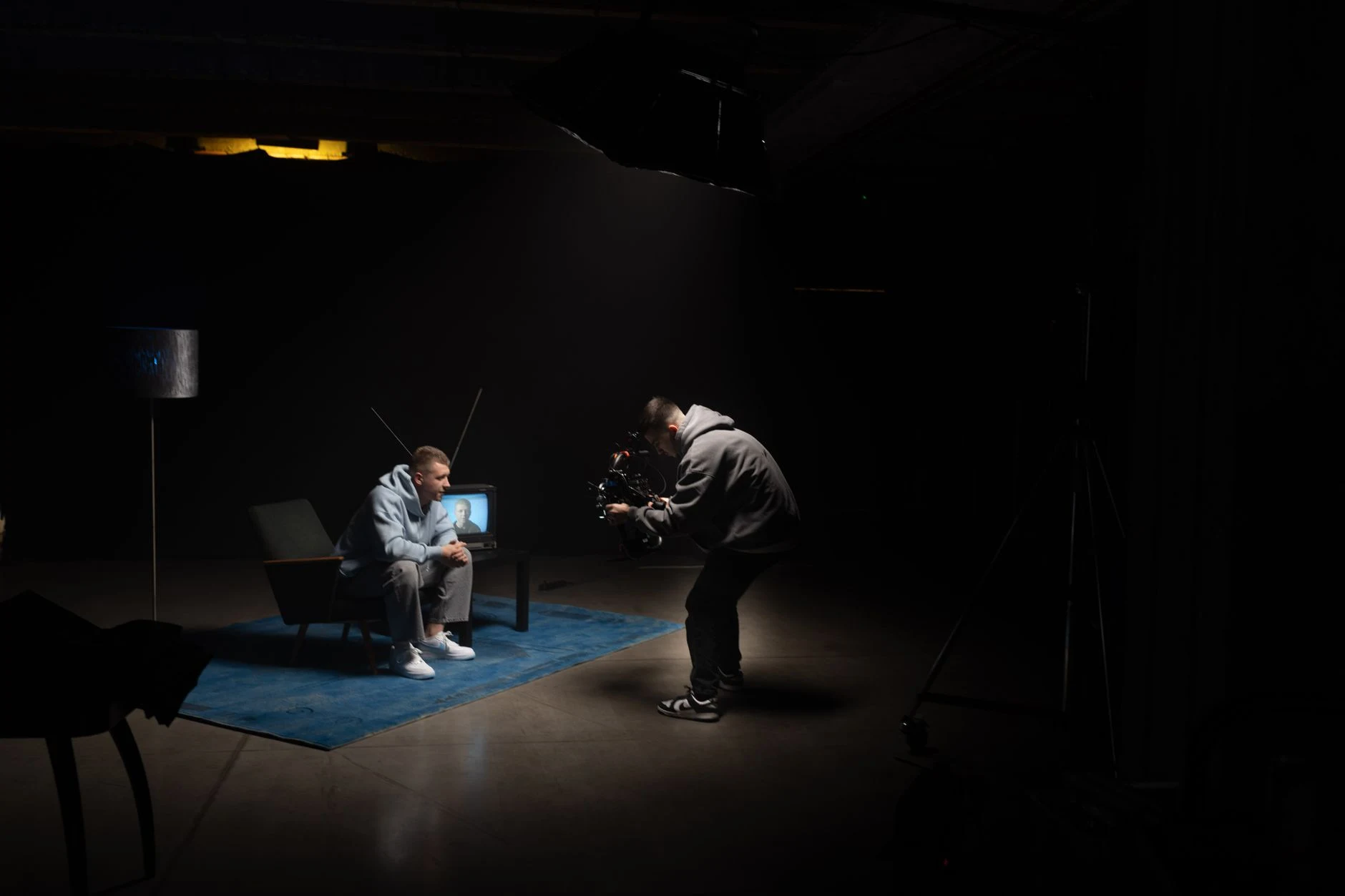 Film production shoot indoors with cinematographer filming an actor sitting, studio lighting.